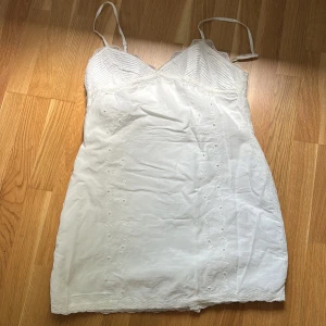 Vit kort klänning med spetsdetaljer - Söt vit kort klänning med tunna axelband och v-ringad byst. Klänningen har broderade blommor och spets längs kanterna för en romantisk vibe.  Lätt och luftig känsla i bomull. Den är från Zara i storlek L men skulle säga att den är mindre i storleken och aitter som en M💕💕💕