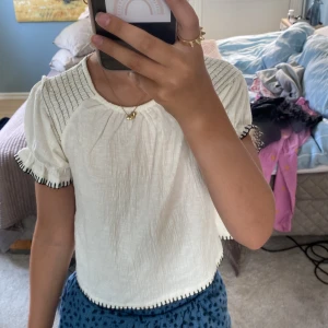 Vit blus med svarta detaljer från Zara - Supersöt vit/beige blus från Zara med puffiga korta ärmar och svarta broderade sömmar längs kanterna. Blusen har rynkade axlar och en luftig, lite boxig passform. Perfekt för en snygg och stilren look.