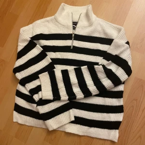 Randig stickad tröja med half zip - Säljer en svartvit randig stickad tröja med half zip och hög krage. Tröjan har långa ärmar och är ribbstickad för extra mysfaktor. Perfekt för dig som gillar en chill och stilren look.