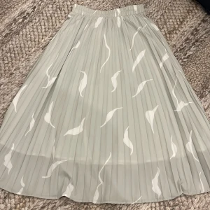 Grön plisserad kjol  - Superfin grön plisserad långkjol från DAZY med vitt mönster. Kjolen har elastisk midja. Storlek S