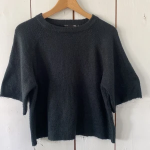 Mörkgrå stickad tröja 157 XS - Mysig mörkblå stickad tröja från 157 i boxig modell. Tröjan har kortare ärmar och en rund halsringning. Perfekt för lager-på-lager och chill dagar. Passar dig som gillar en enkel och avslappnad stil.