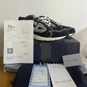 Dior b30 sneakers med vita detaljer - Snygga svarta Dior sneakers med vita och silverfärgade detaljer samt stora CD-loggor på sidorna. Skorna har vit sula, vita snören och meshpaneler för extra komfort. Perfekt för dig som vill sticka ut med exklusiva och trendiga sneakers. Storlek 47