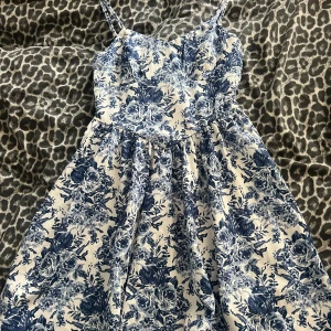 Blåvit blommig sommarklänning - Supersöt blåvit klänning med blommigt mönster och smala axelband. Utsvängd kjol och figurnära överdel ger en feminin siluett. Perfekt för varma dagar och picknickar. Lätt och luftig känsla.