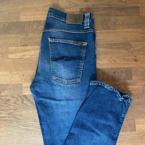 Nudie Jeans Grim Trim Blå jeans - Säljer ett par Grim Trim jeans från Nudie Jeans i klassisk blå tvätt. Jeansen har inte blivit mycket använda och är i princip felfria!