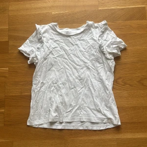 Vit volangtopp från Zara - Säljer en söt vit topp från Zara i storlek S. Toppen har korta ärmar med volangdetaljer som ger en extra touch. Tillverkad i mjuk bomull och har en klassisk rund halsringning. Perfekt för dig som gillar en enkel men ändå trendig stil.