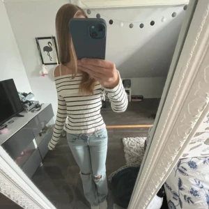 Randig offshoulder tröja i vitt - Supersnygg ribbad offshoulder tröja i vitt med svarta horisontella ränder. Tröjan är figurnära och har långa ärmar. Perfekt för dig som gillar en stilren och trendig look. Materialet känns mjukt och stretchigt, vilket gör den bekväm att bära. Knappt använd.