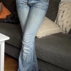 Rock & Republic bootcut jeans med brodyr - Snygga blå bootcut jeans från Rock & Republic med låg midja. Bakfickan har blå broderi och glittriga stenar i form av vingar. Jeansen har klassisk femficksdesign och är gjorda i denim med lätt tvättad look. Köpte dem second hand i LA💗💗