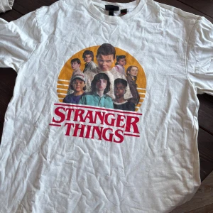 Stranger Things t-shirt vit S - Vit Stranger Things t-shirt från H&M i storlek S. Tryck med karaktärerna från serien och stor röd logga framtill. Klassisk rund hals och korta ärmar. Skön bomullskvalitet, perfekt för dig som älskar serien och vill ha en snygg statement-tee.