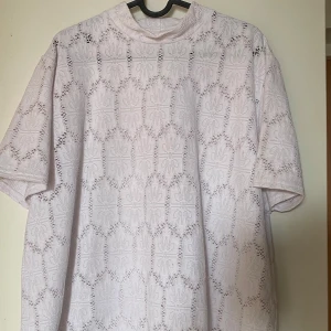 Vit spetsblus från Jacett - Supersöt vit blus från Jacett i storlek XXL. Blusen har korta ärmar, hög hals och är helt täckt av ett broderat spetsmönster med blommiga detaljer. Perfekt för dig som gillar romantisk och luftig stil. Frakt tillkommer