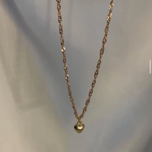 Guldigt halsband med hjärthänge - Snyggt halsband i guldton med tvinnad kedja och ett litet hjärthänge. Perfekt accessoar för att lyfta din outfit med en söt detalj. Passar dig som gillar stilrena smycken med en romantisk touch.