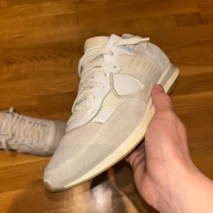 Philippe model sneakers vit - Snygga sneakers i beige och vitt med detaljer i mocka, skinn och mesh. Klassisk siluett med rund tå, platt sula och snörning. Perfekta för dig som gillar stilrena och exklusiva sneakers med lyxig känsla.
