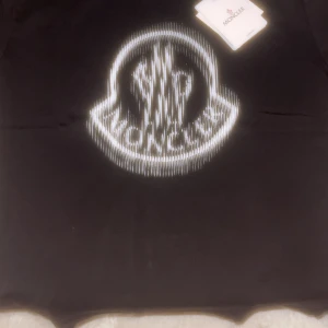 Svart Moncler t-shirt med logga - Svart t-shirt från Moncler med stor vit logga framtill i coolt, grafiskt mönster. Klassisk passform och rund hals. Perfekt för dig som gillar streetstyle och vill sticka ut med ett exklusivt märke.