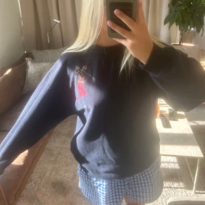 Mörkblå stickad tröja med broderi - Mörkblå stickad tröja med lång ärm och broderad golfspelare i färgglada toner på bröstet. Tröjan har en avslappnad passform och rund halsringning. Perfekt för dig som gillar unika detaljer och sportiga vibbar. Tröjan är köpt i Australien o har storlek 12, vet inte vad det exakt motsvarar men jag har S/M och den passar bra!