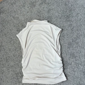 Vit ärmlös linnetopp med rynk från H&M - Säljer en vit linnetopp med ärmlös design och lätt rynkade sidor. Toppen har en mjuk, slät yta och en enkel, rak passform. Från H&M divided. Knappt använd. 
