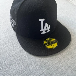 Svart LA Dodgers keps New Era 59FIFTY - ALDRIG ANVÄNT. Snygg svart LA Dodgers keps från New Era 59FIFTY-serien med broderad LA-logga framtill och 1988 World Series-märke på sidan. Klassisk flat peak och MLB-logga bak. 