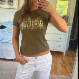 Olivgrön t-shirt med guldtext - Snygg olivgrön t-shirt med korta ärmar och texten 'WILD' i guld och paljettdetaljer framtill. Perfekt till jeans eller shorts.  Passar xs/s/m