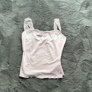 Ljusrosa linnetopp med spets från SHEIN - Supersöt ljusrosa linnetopp från SHEIN i storlek XS. Toppen har breda axelband i spets och en mjuk, glansig finish. Perfekt för lager-på-lager eller som statement-piece. Snygg vågig kant nertill och romantisk känsla med spetsdetaljer.