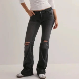 Svarta bootcut jeans med slitningar - Snygga svarta jeans med bootcut passform och slitna detaljer vid knäna. Jeansen har låg midja och klassisk femficksdesign. Perfekta för dig som gillar en avslappnad och trendig look. Materialet är mjukt denim som sitter skönt hela dagen.