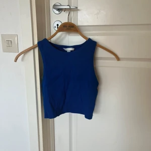 Blå croppad linnetopp - Snygg blå croppad linnetopp med breda axelband och rund halsringning. Perfekt för varma dagar eller att styla lager på lager. Enkel och stilren design som är lätt att matcha med jeans eller kjol.