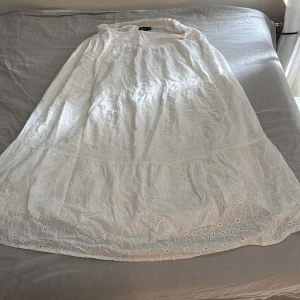 Vit långklänning från Boohoo strl 44 - Superfin vit långkjol från Boohoo med broderade detaljer och lätt volang nertill. Klänningen har en luftig passform och är perfekt för varma dagar. Tillverkad i bomull med vackert hålbroderi som ger en romantisk känsla. För referens jag är 179 cm lång!