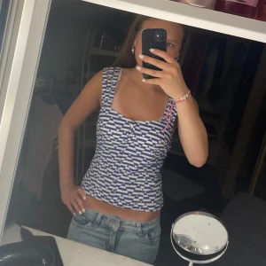 Randig topp - Snygg linnetopp med breda axelband och blåvitt grafiskt mönster. Toppen har en croppad passform och fyrkantig ringning framtill. Perfekt till jeans eller kjol för en fräsch look.