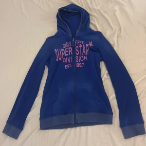 Blå hoodie från Red & Blue - Blå hoodie från Red & Blue med rosa tryck på bröstet. Tröjan har luva, dragkedja framtill och två fickor. 🩷💙