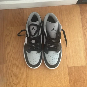 Nike Air Jordan 1 Low svart/grå/vit - Säljer ett par Nike Air Jordan 1 Low i svart, grått och vitt. Skorna har klassisk Jordan-logga på plösen, svart snörning och perforerad tå. Ovandelen är i skinn och syntet, har bara använt dom två gånger i väldigt bra skick 