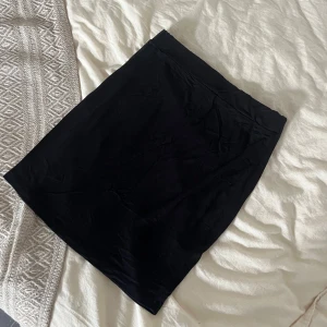 Svart enkel kortkjol - Svart, stilren och basic kortkjol med rak passform. Kjolen är enfärgad och har en mjuk, stretchig känsla som gör den bekväm att bära. Perfekt att matcha med en crop top eller oversized hoodie för en chill look.