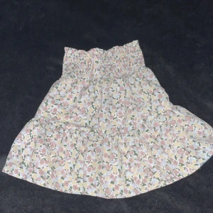 Blommig volangkjol från Name It - Supersöt kort kjol från Name It med blommigt mönster i pastelliga toner av rosa, gul och grön. Kjolen har bred smock i midjan och volang nertill för extra flowig känsla. Perfekt för dig som gillar en romantisk och somrig stil. Stretchig 