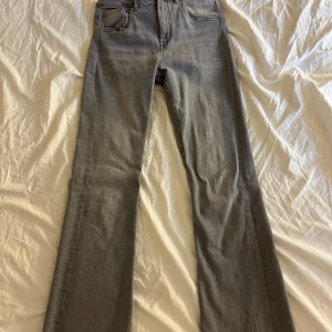 Grå bootcut jeans med låg midja - Snygga grå jeans med bootcut-modell och låg midja. Klassisk femficksdesign och bälteshällor. Jeansen har en rak passform upptill och blir vidare nedtill för en riktigt chill vibe. Perfekta till sneakers eller boots.