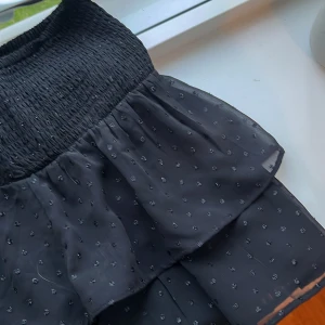 Svart volangkjol med små prickar - Supersöt svart kortkjol med volanger och små diskreta prickar. Resår i midjan för skön passform och lätt, luftig känsla. Perfekt att styla med en crop top eller stickad tröja. Kjolen har en flowy look och är riktigt bekväm. Inga tecken på användning 