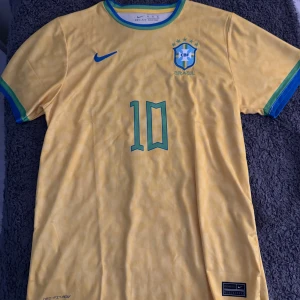 Brasilien Neymar 10 Nike fotbollströja XL - Gul Brasilien fotbollströja från Nike med Neymar och nummer 10 på ryggen. Tröjan har gröna och blå detaljer vid krage och ärmslut, samt CBF-emblem på bröstet. Tillverkad i Dri-Fit material som andas, perfekt för match eller träning.