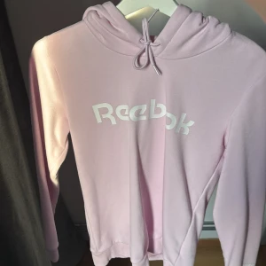 Ljusrosa hoodie från Reebok XS - Supermjuk ljusrosa hoodie från Reebok i storlek XS. Tröjan har huva med snörning och stor vit logga framtill. Perfekt för chill dagar eller när du vill ha en sportig look. Tillverkad i bomullsmix för extra komfort. Tyvärr inte min stil längre!☺️