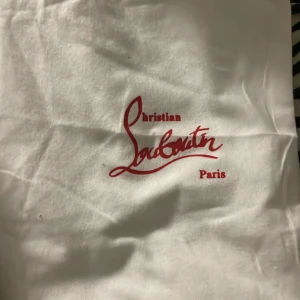 Christian Louboutin svarta - Svarta sneakers från Christian Louboutin i mocka med ikonisk röd sula och svarta nitar på tån. Skorna har snörning och rund tå, samt exklusiva detaljer som signatur på sulan och insidan. Perfekta för dig som vill sticka ut med lyxig streetstyle. Man får med kvitto ( 2 st ) och ett present kort 