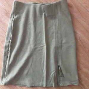 Olivgrön kjol från Gina Tricot XS - Snygg olivgrön kortkjol från Gina Tricot i storlek XS. Kjolen har en stilren design med en liten slits framtill som ger en extra touch. Perfekt att matcha med en crop top eller oversized hoodie för en chill look.