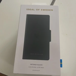 Svart plånbok skal Ideal of Sweden - Snygg svart plånbok skal från Ideal of Sweden, designad för iPhone 12 Pro Max. Stilren och minimalistisk look med magnetstängning och plats för kort. Perfekt accessoar för dig som vill ha både skydd och stil.