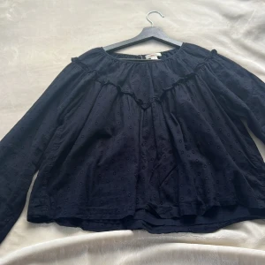 Mörkblå blus med volang från Gina Tricot - Supersöt mörkblå blus från Gina Tricot med diskret prickigt mönster och volangdetalj över bröstet. Blusen har lång ärm och rund halsringning, perfekt för dig som gillar en romantisk och chill stil.