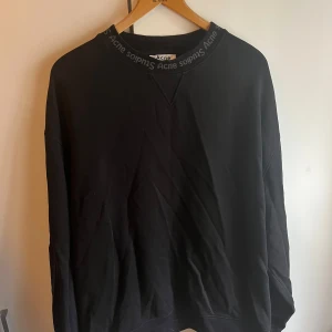 Svart sweatshirt från Acne Studios - Svart sweatshirt från Acne Studios med logga runt halsringningen i bra skick. I storlek oversized L så passar bra för även XL. Ny pris ungefär 1800. Tröjan är i mycket bra skick men är använd i drygt 1 år därför är priset lägre. Dm mig för att diskutera priset :)