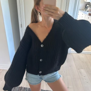 Svart kofta från NA-KD med stora knappar - Mysig svart kofta från NA-KD med oversized passform, stora silvriga knappar och ribbad stickning. Koftan har v-ringning och långa, vida ärmar. 