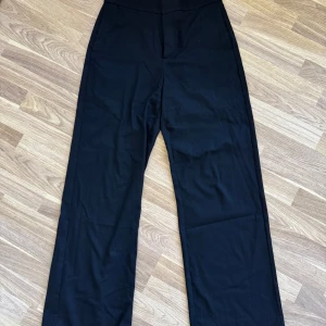 Svarta kostymbyxor från Lindex - Stilrena svarta kostymbyxor från Lindex i modellen Lykke. Byxorna har hög midja och raka, vida ben för en clean och modern look. Perfekta att matcha med en crop top eller oversized skjorta. Materialet känns mjukt och bekvämt.