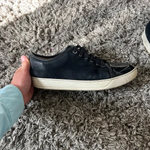 Blå sneakers från Lanvin med glans - Snygga blå sneakers från Lanvin med ovandel i mocka och detaljer i blankt skinn framtill. Klassisk vit sula och blå skosnören. Perfekta för dig som gillar stilrena och exklusiva sneakers med en lyxig touch.