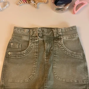 Grön jeanskjol - Snygg grön jeanskjol med två stora framfickor, dubbla knappar i midjan. Kjolen har även två bakfickor och en klassisk jeanslook. Perfekt för dig som gillar en enkel men cool stil. Säljs då den är förliten 🥰