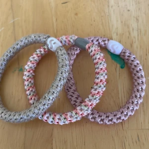 3-pack flätade armband i pastell - Säljer tre chunky flätade armband i pastelliga färger: ett i skimrande silver, ett i rosa och ett mixat i rosa, silver och vitt. Alla har en cool pärldetalj som lås. Perfekta för att ge din outfit en färgklick och lite extra attityd.