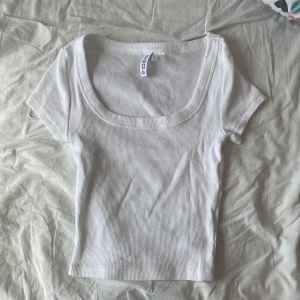 Vit ribbad croppad topp - Superfräsch vit croppad topp från H&M Divided med ribbad struktur. Toppen har korta ärmar och en djup, fyrkantig urringning som ger en snygg och trendig look. Katt finns i hemmet!