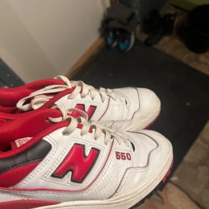 New Balance 550 vita och röda sneakers - Säljer ett par New Balance 550 sneakers i vitt och rött med svarta detaljer. Klassisk retrodesign med tydlig N-logga på sidan, snörning och lågt skaft. Ovandel i skinn och syntet, perforerade partier för extra ventilation. Perfekta för dig som gillar streetwear.