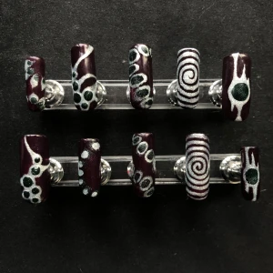 Handmålade lösnaglar - Set med 10 lösnaglar i vinrött med handmålade mönster i silver och mörkgrönt. Naglarna har olika motiv som spiraler, prickar och abstrakta linjer. Långa med glansig finish, perfekta för dig som vill sticka ut med unika naglar. Billigare pris då jag inte blev helt nöjd med resultatet.