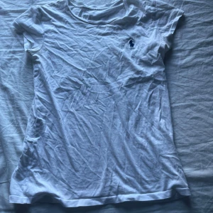 Vit t-shirt ralph lauren  - Vit t-shirt från Polo Ralph Lauren med klassisk marinblå broderad logga på bröstet. T-shirten är i mjuk bomull, har rund hals och korta ärmar. Enkel och stilren modell som passar perfekt till jeans eller shorts. Står inte storlek men jag skulle säga att den passar till xs 