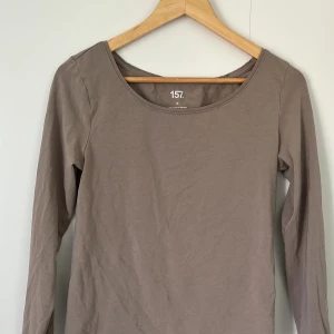Beige långärmad tröja från 157 - En basic beige långärmad tröja från 157 i mjuk bomullsmix med rund halsringning. Perfekt att styla med jeans eller kjol för en clean och enkel look. Tröjan är i stretchigt material som sitter skönt mot kroppen.