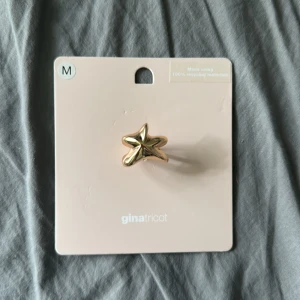Guldig stjärnring från Gina Tricot - Cool ring i guldig metall från Gina Tricot, formad som en stjärna. Statement piece som verkligen sticker ut och ger en trendig vibe till din look. Perfekt för dig som gillar unika accessoarer och vill addera lite extra bling till outfiten. Prefekt nu för sommar! Självklart inte använd! 