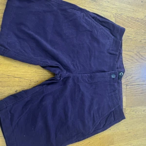 Mörklila shorts från WeSC - Snygga mörklila shorts från WeSC med klassisk passform och raka ben. De har bälteshällor, sidofickor och bakfickor med knappdetalj. Perfekta för sommardagar och chill häng. Materialet känns som bomull och ger en skön känsla mot huden.